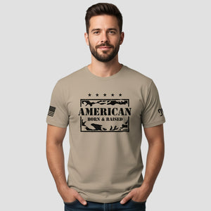 Man wearing a beige t-shirt with 'American Born & Raised' graphic design on a light gray background