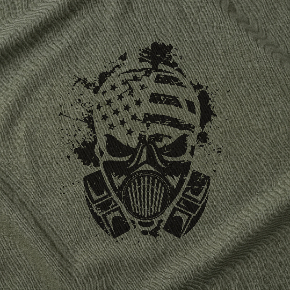 Close-up of the American Fighter Skull T-Shirt front print on Military Green: the gas mask skull, its respirator and the stars and stripes across the cranium in black ink splatter (digitally composited print visualization, not a photograph)