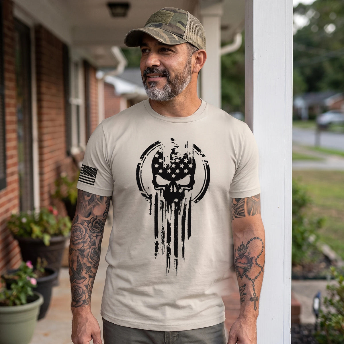 Man in a camo cap wearing the Sand American Warrior Skull T-Shirt on the front porch of a brick house