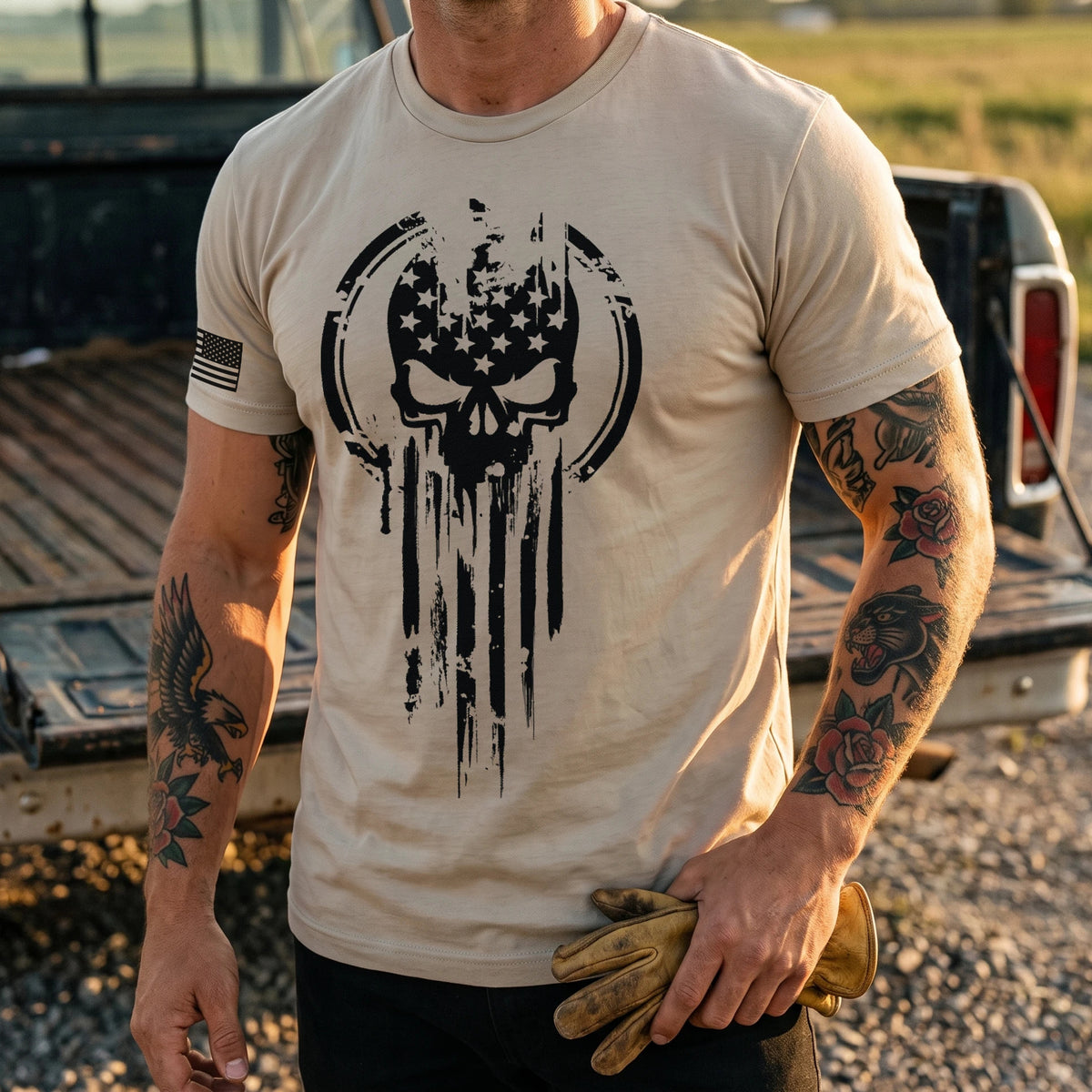Close-up of the skull and flag chest print on the Sand American Warrior Skull T-Shirt, worn at a pickup truck tailgate at golden hour