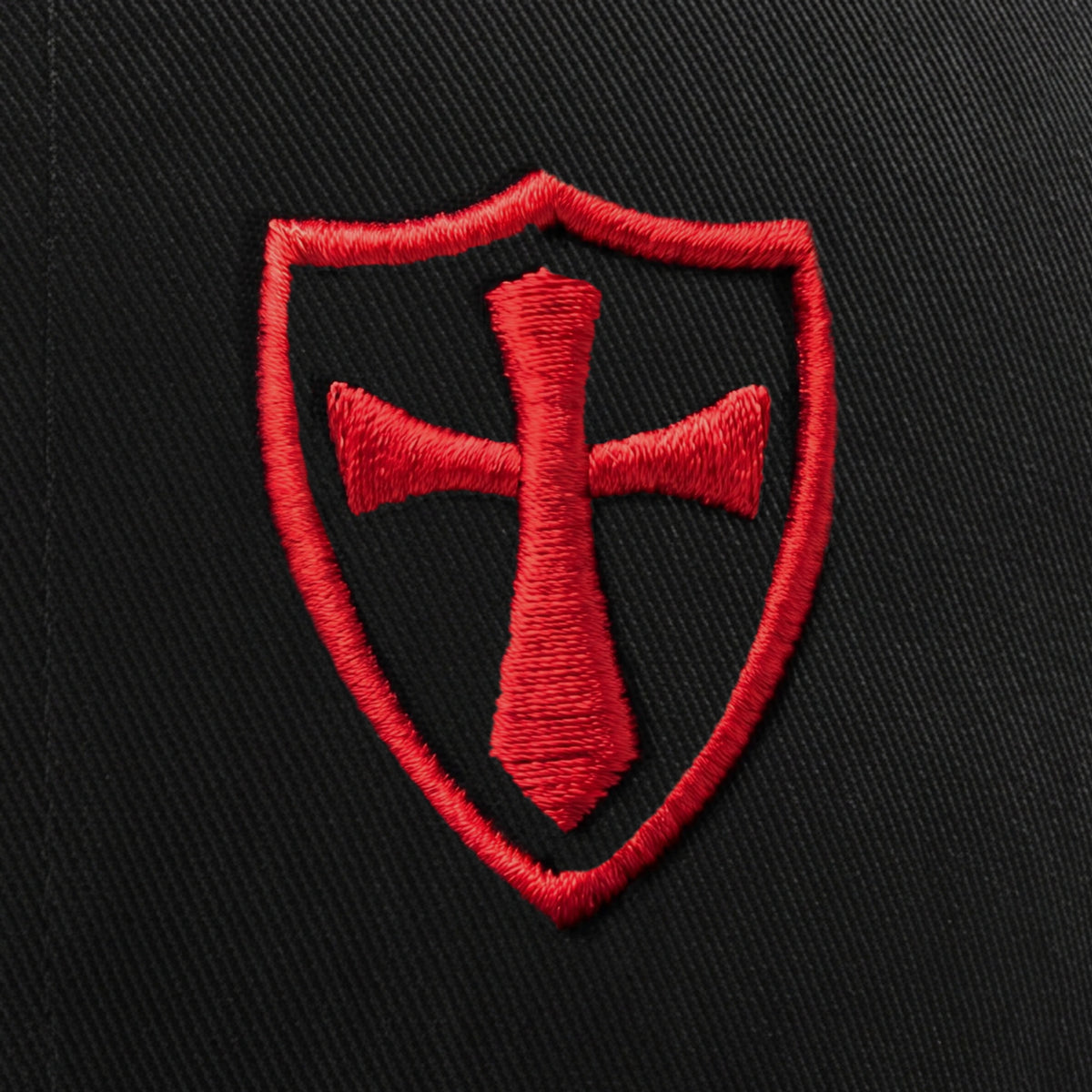 Close-up of the raised red 3D puff Crusader shield and cross embroidery on the black trucker hat