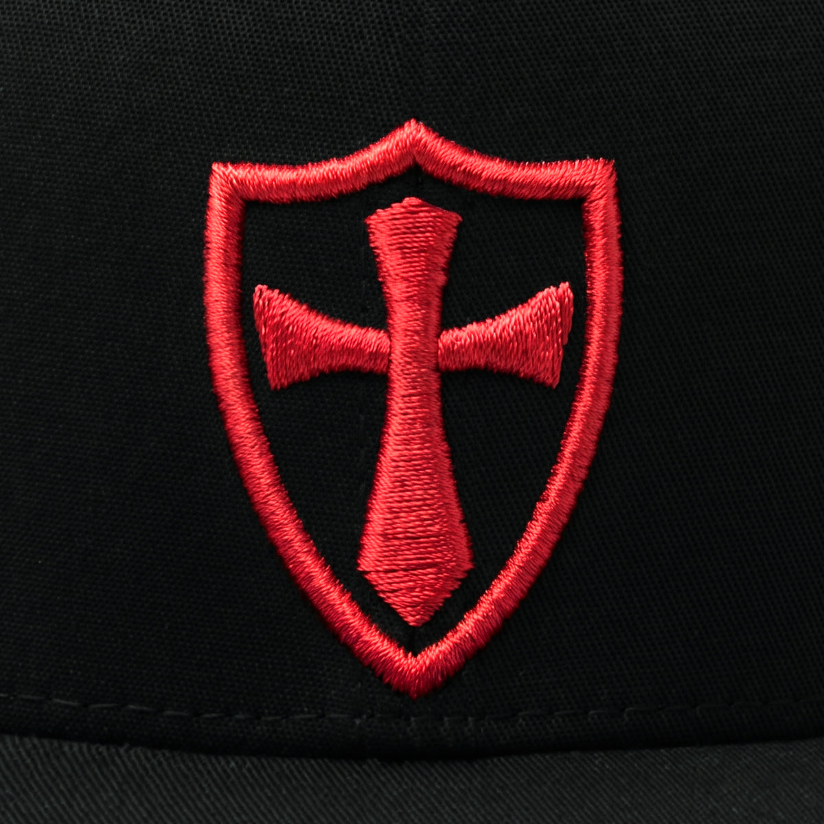 Close-up of the raised red 3D puff Crusader shield and cross stitching on the black Crusader Cross Stretch Fit Cap