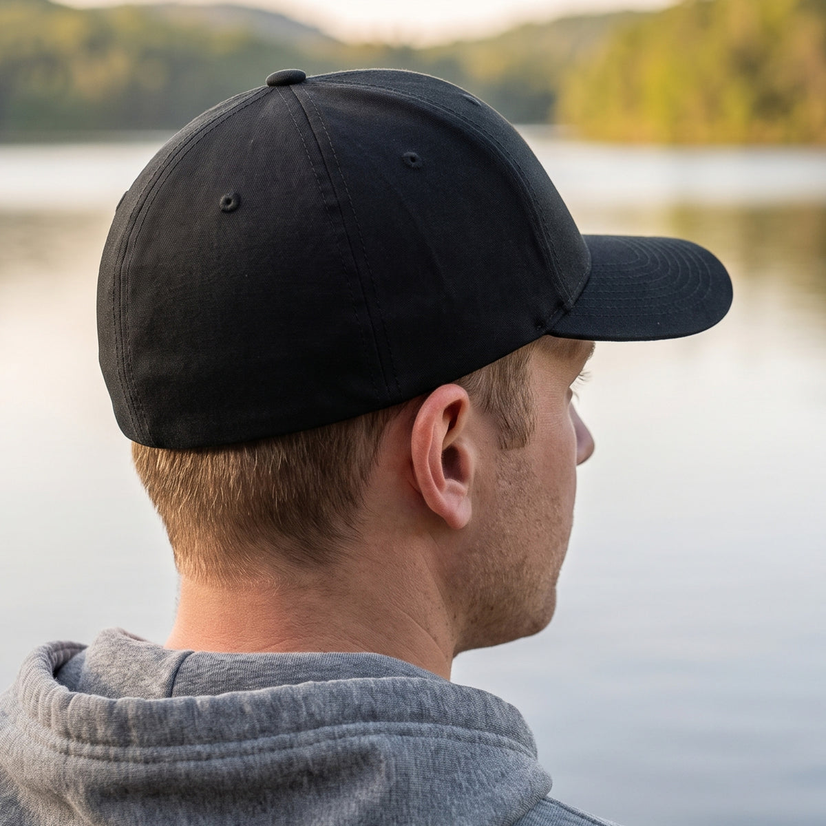 Rear three-quarter view of the black Dion Wear stretch fit cap on a man by a lake: clean, closed stretch-fit back with no embroidery
