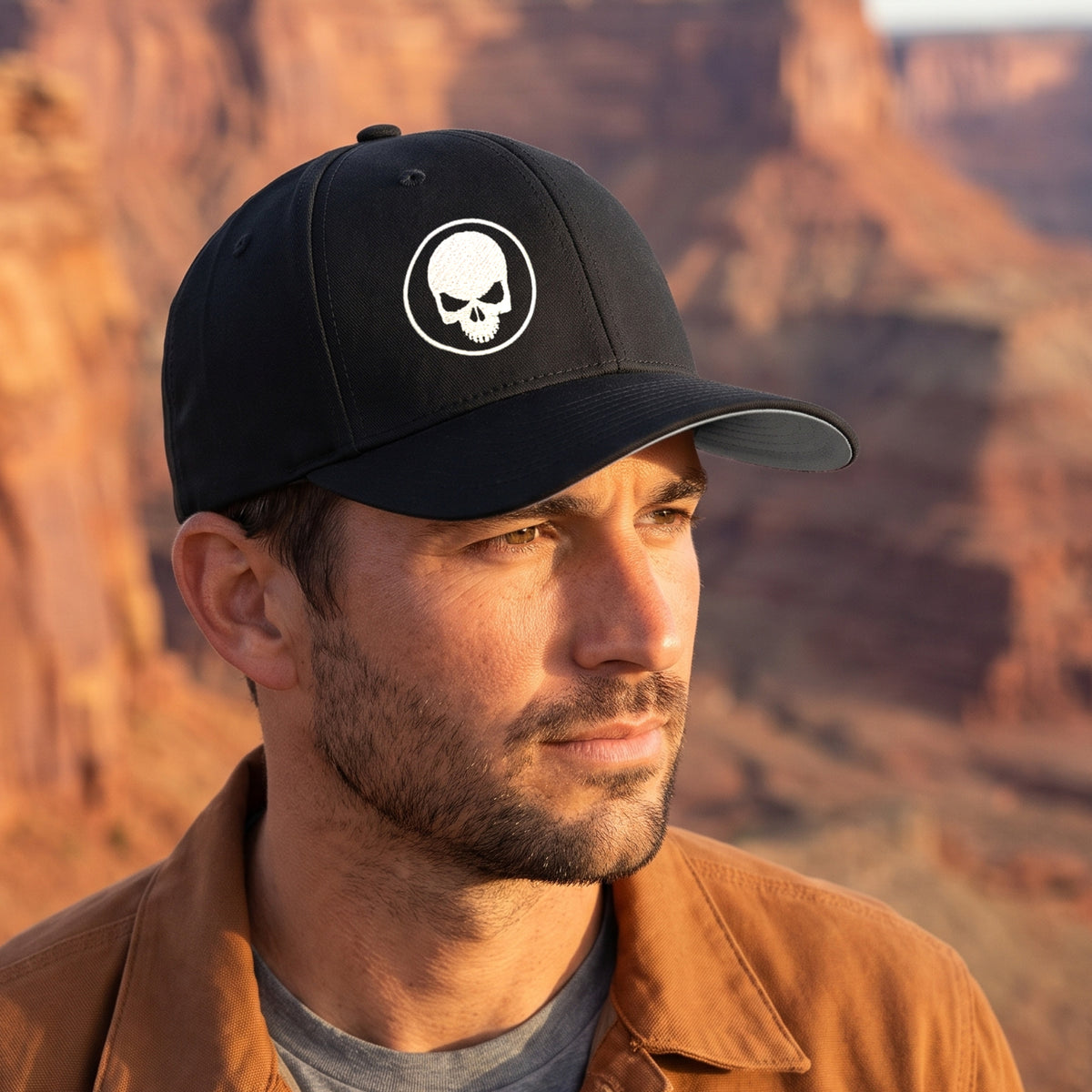 Man at a red-rock canyon overlook at golden hour wearing the black Skull Stretch Fit Cap with the white embroidered skull, front three-quarter view