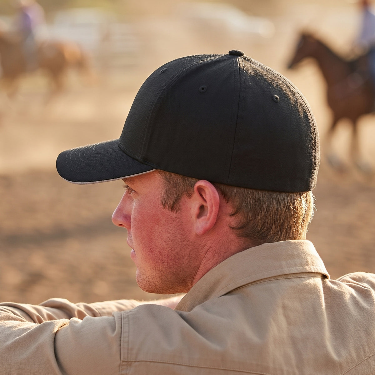 Rear three-quarter view of the black Skull Stretch Fit Cap on a man at a rodeo arena fence: clean, closed stretch-fit back with no embroidery