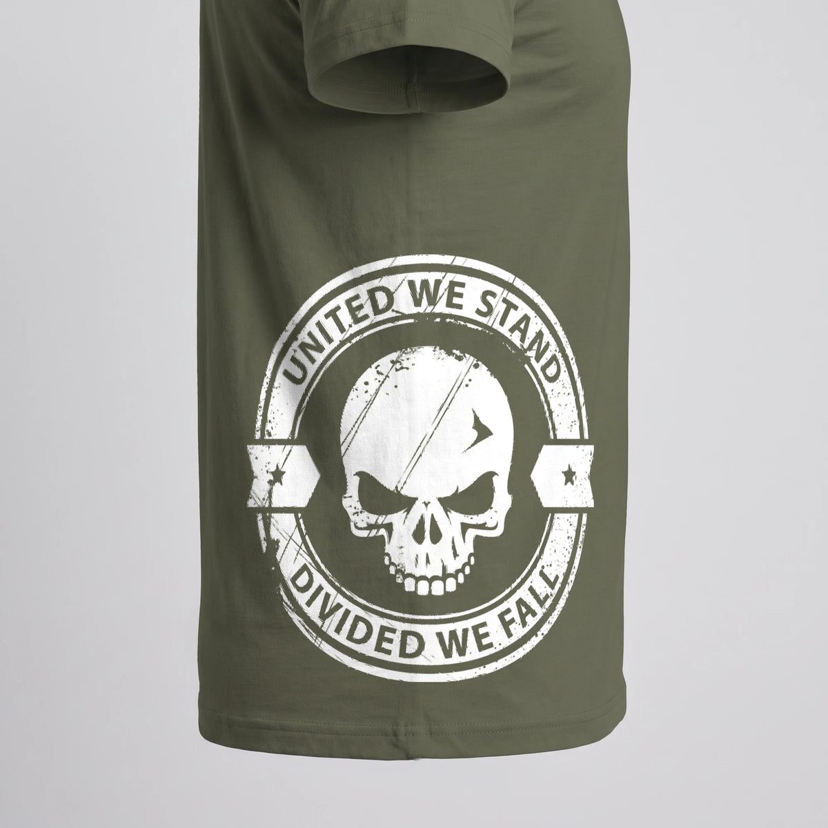Close-up of the United We Stand Skull T-Shirt side print on Military Green: skull inside a ring reading UNITED WE STAND and DIVIDED WE FALL, with banners and stars, wrapping around the right side above the hem (digitally composited print visualization, not a photograph)